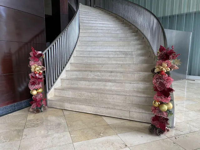 Escalera curva de mármol con dos guirnaldas navideñas en burdeo y dorado