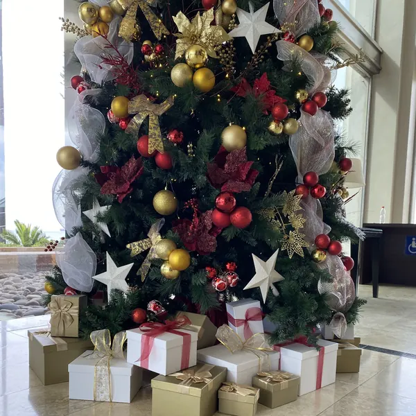 Regalos decorativos dorados y blancos al pie de un árbol de Navidad