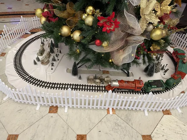 Tren navideño y aldea nevada en miniatura alrededor de la base de un árbol