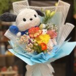 Amigo Mágico Bouquet con peluche de Pochacco y flores vibrantes, envuelto en papel azul.