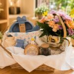 Canasta de regalo para bebé y mamá con flores, tazón dorado y ajuar de bebé