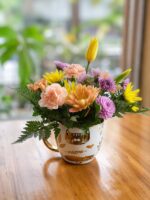 Arreglo de flores frescas en tonos pastel en taza blanca con diseños dorados