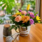 Taza blanca con diseños dorados rellena de flores pastel, frasco de té e infusor