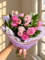 Ramo redondo de ranúnculos rosados con ruscus, envuelto en papel lila con cinta rosada – Encactus Viña del Mar