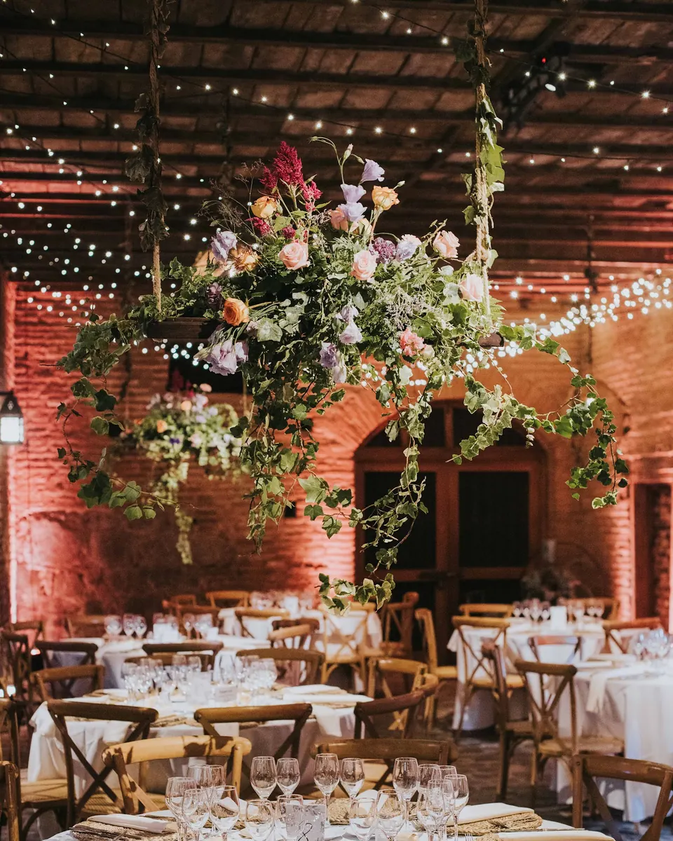 Instalación floral aérea de rosas, lisianthus y hiedra sobre las mesas de una bodega de ladrillo, montaje de Encactus